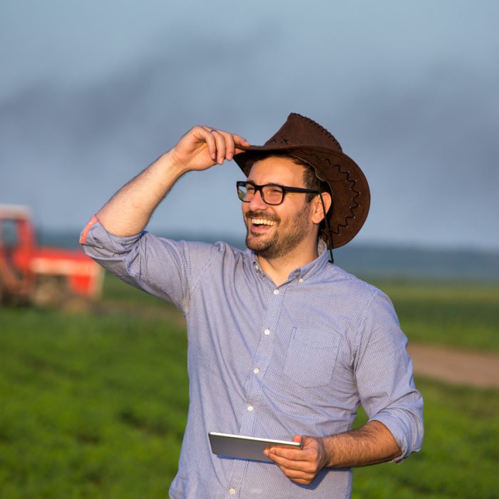 Handsome farmer with hat standing in soybean field in front of tractor